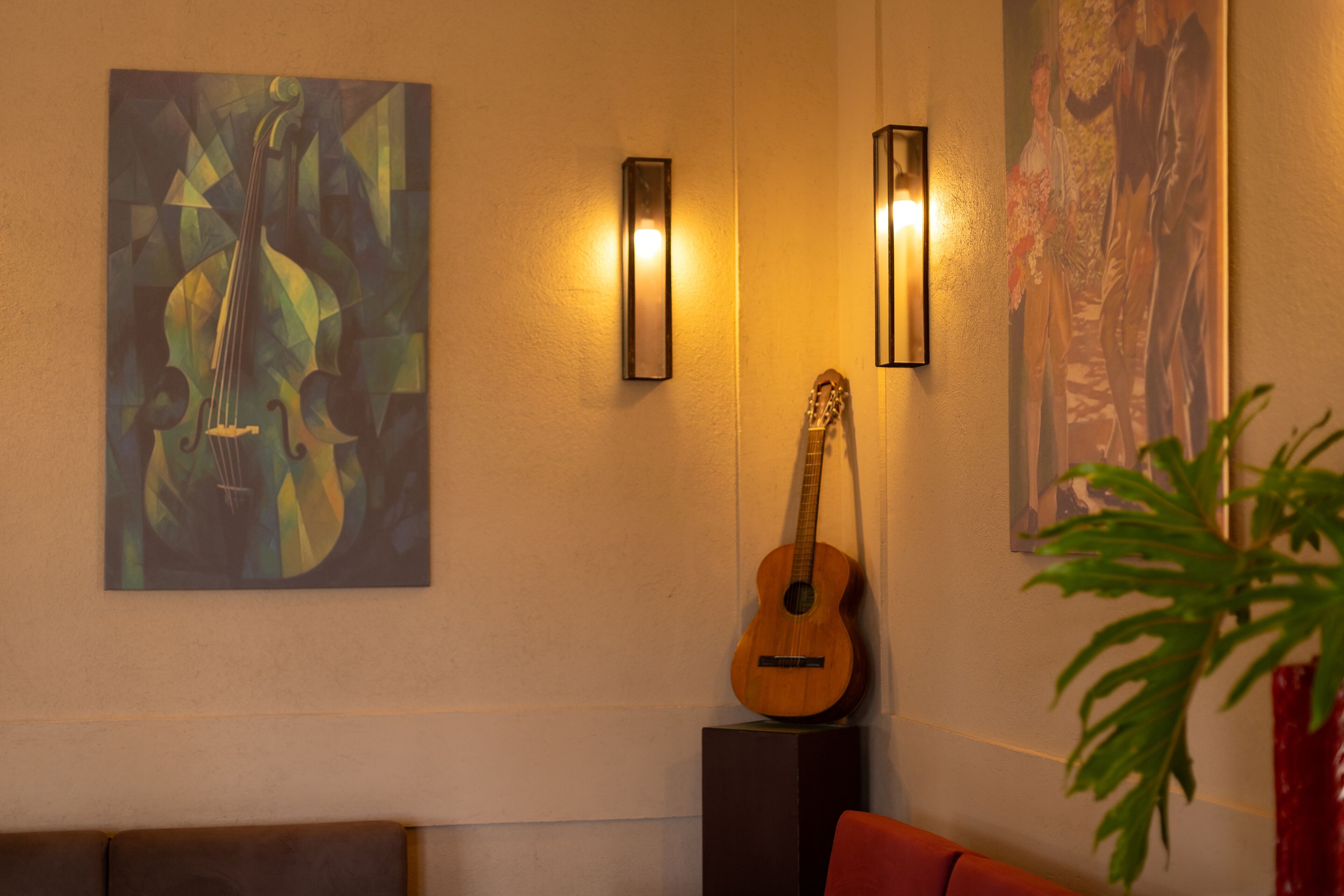A room with a couch, a guitar, and two wall-mounted light fixtures.