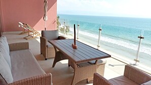 Un balcon agrémenté de meubles en osier, d’une table en bois et offrant une vue sur la plage.