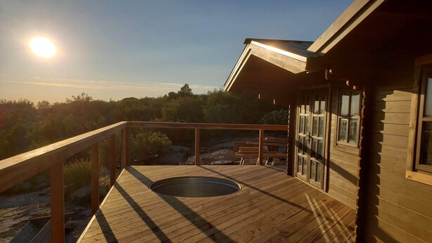 Een houten terras met een jacuzzi, houten leuningen en uitzicht op het landschap.