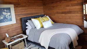 Een houten slaapkamer met een bed, kussens, een nachtkastje, een lijst met een foto en een plafondventilator.