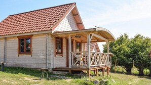 Une cabane en bois avec un toit recouvert de tuiles rouges, une véranda dotée de balustrades en bois et une petite brouette devant.