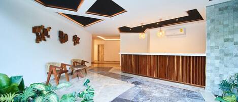Una moderna recepción con un mostrador de madera, una zona de estar con sillones y un piso de baldosas.