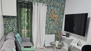 Un salon moderne avec un canapé gris, une petite table ronde, un téléviseur et un mur orné d’un motif végétal.