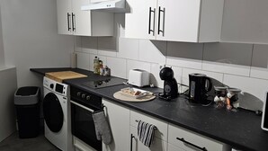 Une cuisine moderne avec des meubles blancs, un lave-linge, une cuisinière et une machine à café.