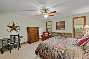 A bedroom with a bed, a desk, a chair, a star decoration, a ceiling fan, and a painting.