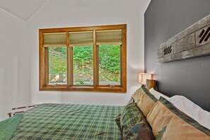 Une chambre avec une grande fenêtre, un lit avec une literie verte et un luminaire fixé au mur.