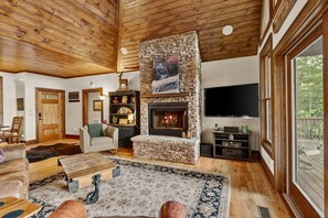 Un salon chaleureux avec une cheminée en pierre, un plafond en bois et une grande fenêtre donnant sur une terrasse.
