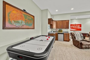 A room with a pool table, a kitchen area, and a living room with a leather sofa.