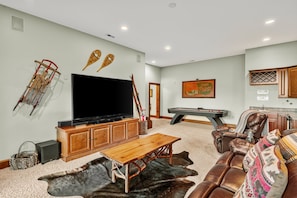 A living room with a flat-screen TV, wooden entertainment unit, and a pool table.