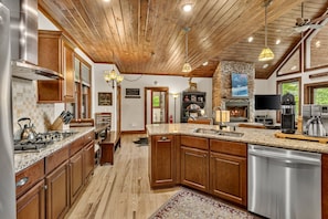 A spacious kitchen with wooden cabinets, granite countertops, a built-in stove, and a stone fireplace.