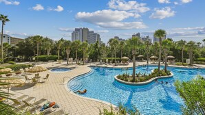 A resort pool area with multiple swimming pools, lounge chairs, and palm trees.