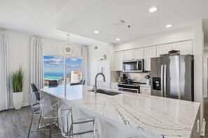 A modern kitchen with a large island, stainless steel appliances, and a view of the ocean.