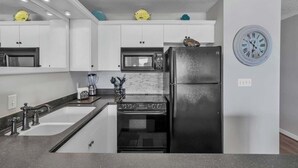 A kitchen with white cabinets, a black refrigerator, a microwave, a stove, and a sink. - Direct Gulf Views, Private Pool, Sleeps 4 (Fort Walton Beach)