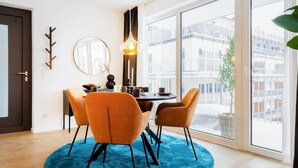 Un comedor moderno con una mesa redonda, dos sillas naranjas, un tapete azul, un espejo y una lámpara colgante.