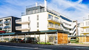 Un edificio de varios pisos con balcones, una zona de estacionamiento techada y un contenedor de basura visible.