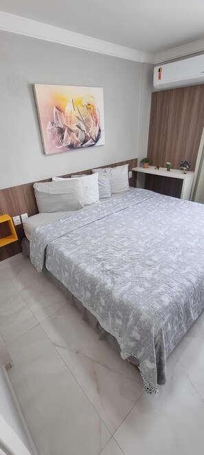 A bedroom with a large bed, a nightstand, a wall-mounted air conditioner, and a small potted plant.