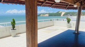 A covered outdoor area with a view of the sea and a mountain.
