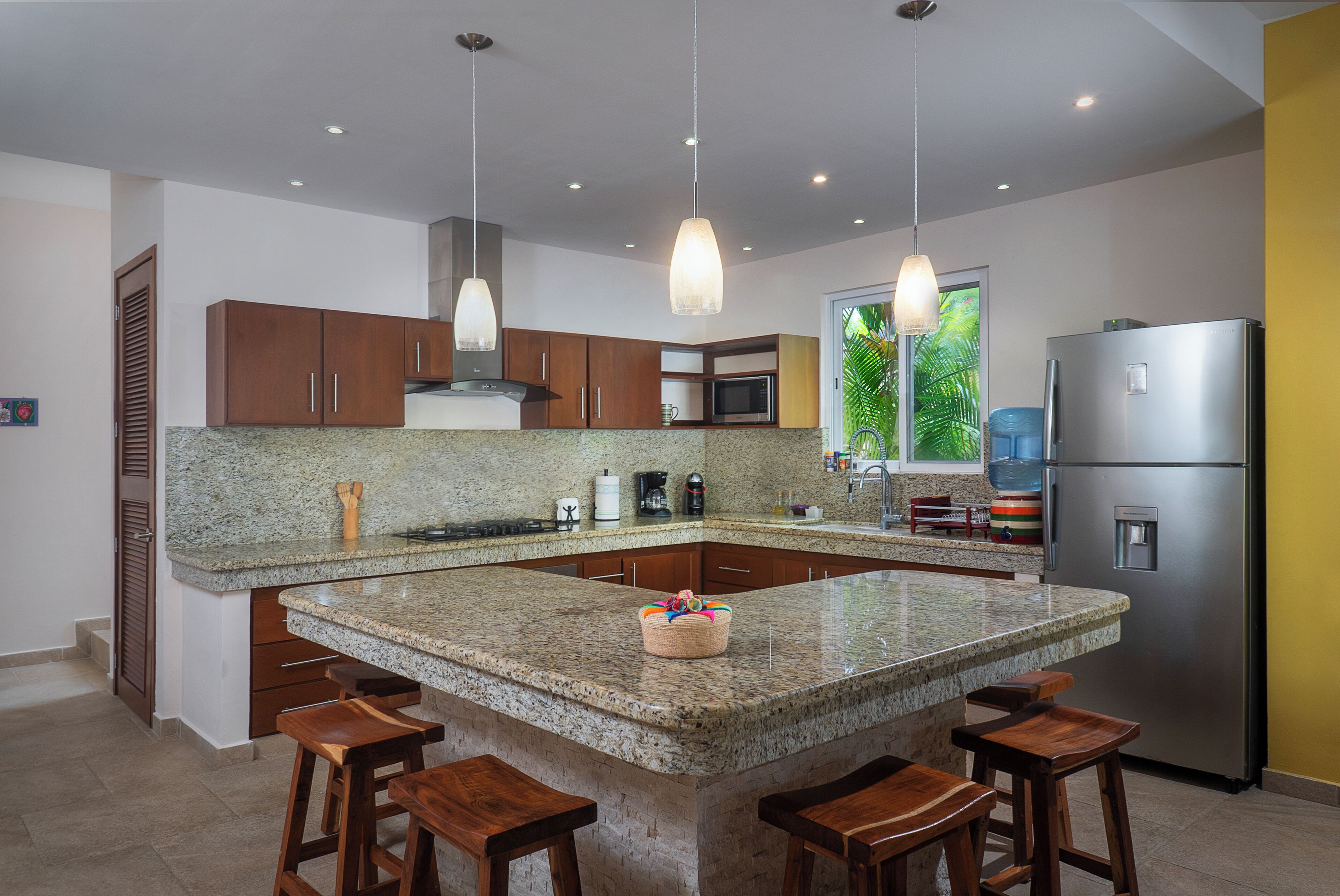 Eine moderne Küche mit Granit Arbeitsplatten, Holzschränken, Edelstahlgeräten und Pendelleuchten.