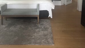 Une chambre à coucher comprenant un lit, des tables de chevet, un ventilateur de plafond, un tapis et une porte donnant sur une autre pièce.