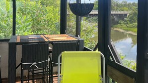Un espace extérieur abrité, aménagé avec une table et des chaises, de grandes fenêtres et des jardinières suspendues.