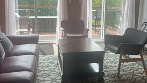 Un salon confortable avec un plafond en bois, un ventilateur de plafond, un grand climatiseur, un canapé, une table et deux chaises.