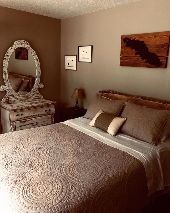 Une chambre à coucher avec un grand lit, une commode avec un miroir, une table de chevet avec une lampe et deux tableaux encadrés accrochés au mur.
