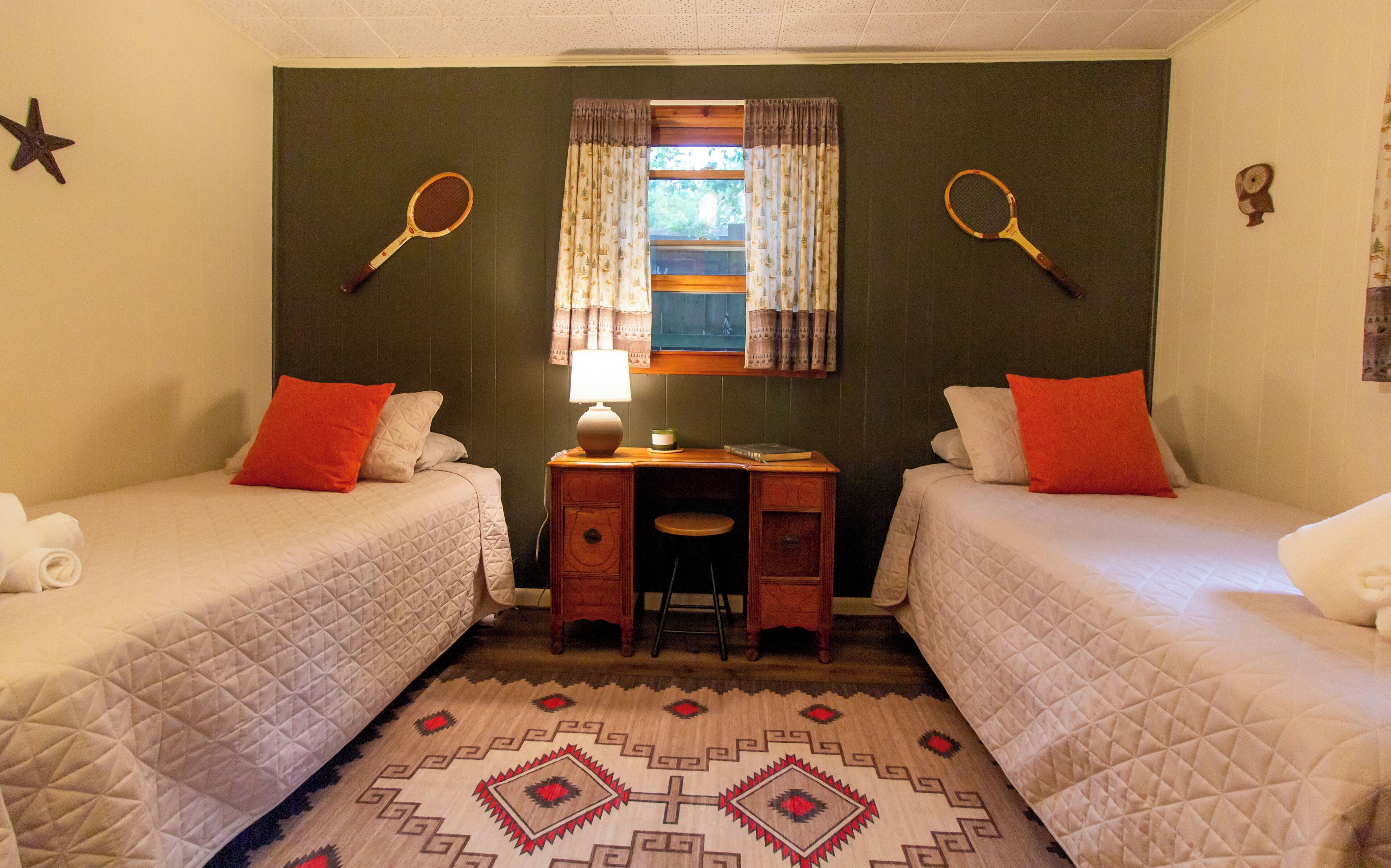 A room with two beds, a desk, and a window with curtains.