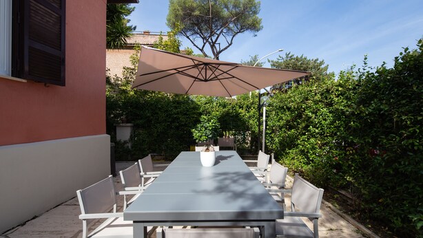 A patio with a table and chairs, a large umbrella, and a tree in the background. - Exquisite Historical Villa in Rome..,Where Elegance Meets History (Roma)