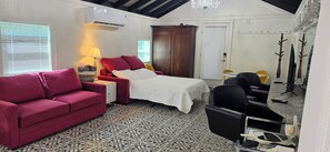 A room with a bed, a red sofa, a small table with a lamp, a TV, and a mirror. - The Elderberry Studio/Check Availability for discounted rates Code: FALL26 (Wanchese)