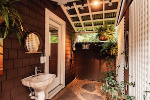 A bathroom with a sink, toilet, and shower area, surrounded by wooden walls and a wooden fence. - Waterfront, Studio and Gardens, Huge grass lawn, Dogs Ok, with fee (Wanchese)