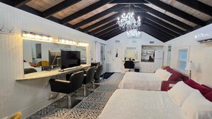 A hotel room with a bed, a desk with a computer, a mirror, a chandelier, and a kitchenette. - The Elderberry Studio (Wanchese)