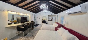A hotel room with a bed, a desk with a computer, a mirror, a chandelier, and a kitchenette. - The Elderberry Studio (Wanchese)