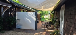 A patio area with a covered seating area, a white privacy screen, and a garden view. - The Elderberry Studio (Wanchese)