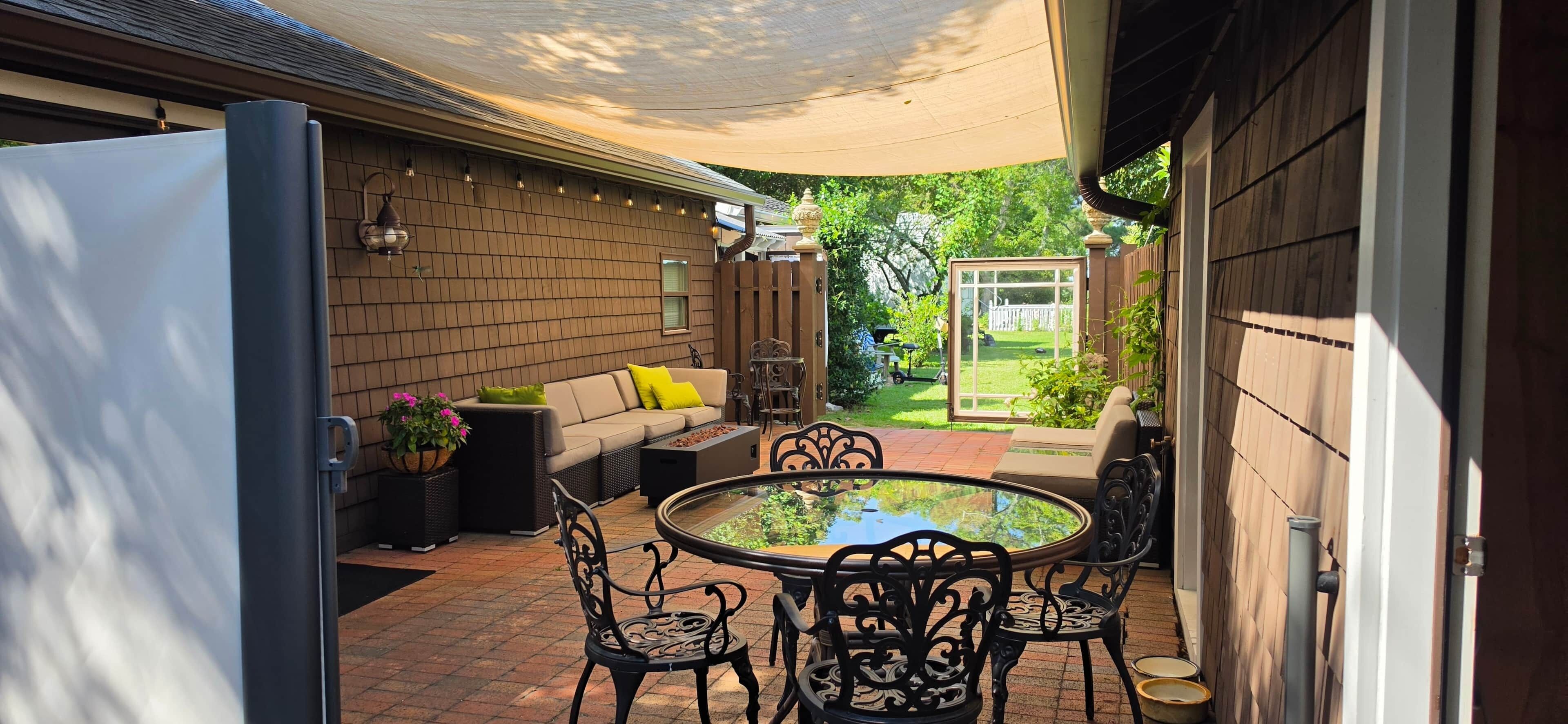 Une terrasse extérieure avec une table ronde et des chaises, un canapé avec des coussins et un sol en briques.