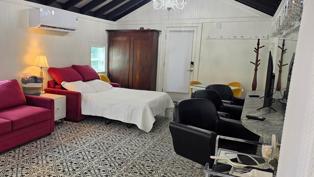 A room with a bed, a red sofa, a desk, a chair, and a TV. - The Elderberry Studio (Wanchese)
