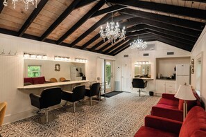 Un salón con un espejo grande, sillas de peluquería negras y un sofá rojo.