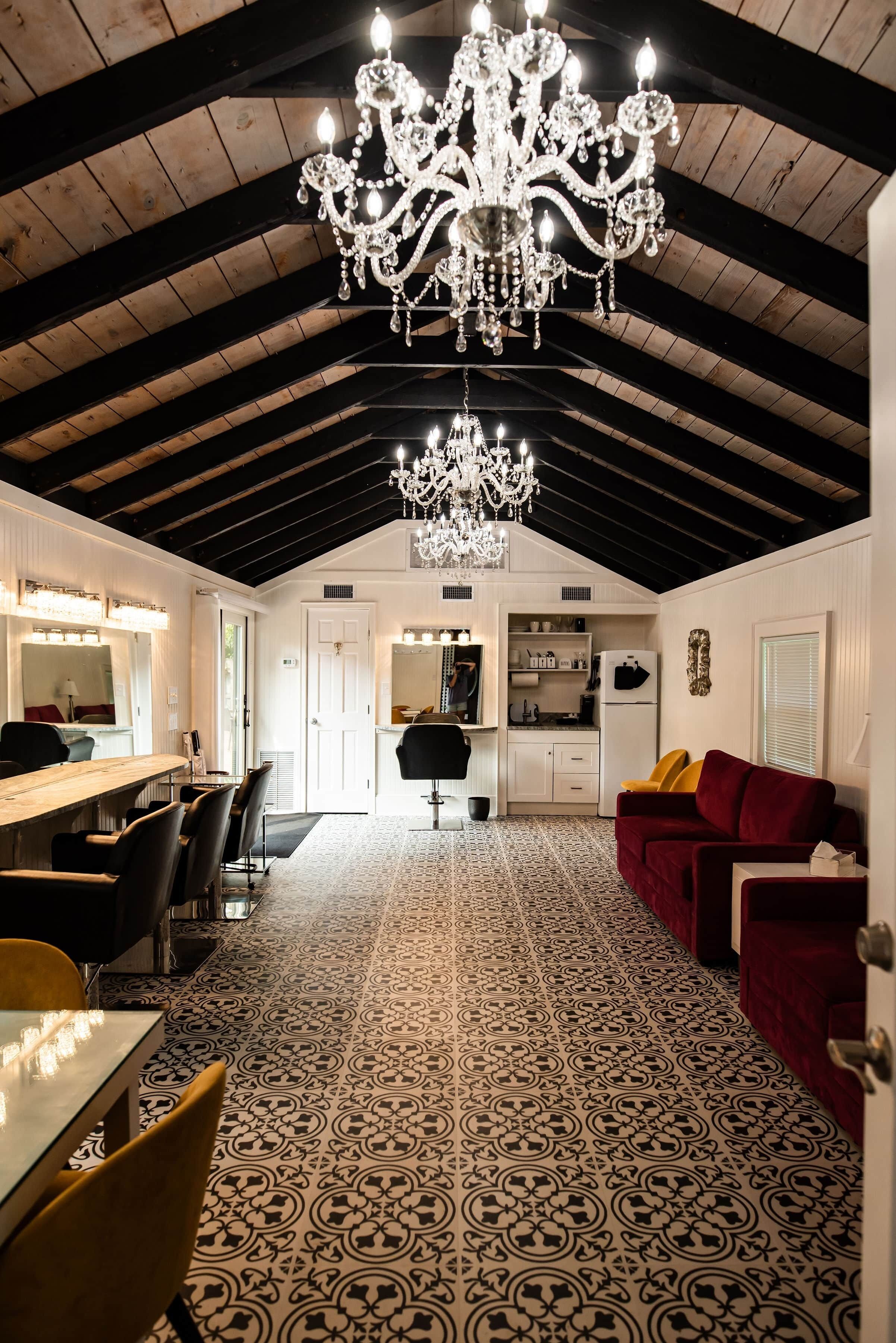 A spacious room with a high ceiling, a chandelier, a dining area with a long table and chairs, and a patterned floor.