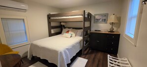Ein Etagenbett mit weißer Bettdecke, eine Nachttischlampe, ein kleiner Schrank und ein Fenster mit Jalousien.