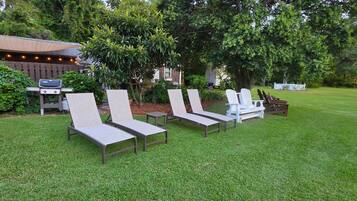 A grassy outdoor area with lounge chairs and a barbecue grill.