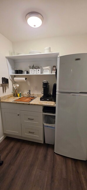 Eine Küche mit einem weißen Kühlschrank, einer Kaffeemaschine und einem Mülleimer.