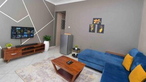 Ein modernes Wohnzimmer mit einem blauen Sofa, einem Holztisch und einem an der Wand befestigten Flachbildfernseher.