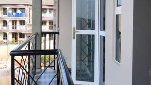 Ein Balkon mit Metallgeländer, einer Glastür und Blick auf ein mehrstöckiges Gebäude.