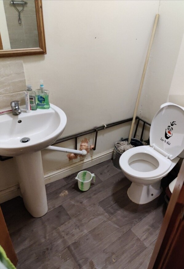 A bathroom with a sink, toilet, and a mop leaning against the wall.