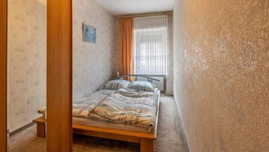 A bedroom with a bed, a radiator, a window with curtains, and a door. - Apartment 'Ferienwohnung Im Harz' with Wi-Fi (Harzgerode)