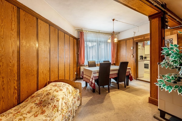 Una habitación con paneles de madera, una cama con ropa de cama floral, una mesa de comedor con sillas y una planta colgante.