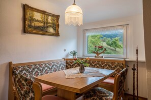 Ein Essbereich mit Tisch, Sitzbänken, einem Chandelier, einem Fenster mit Ausblick und einem gerahmten Gemälde an der Wand.