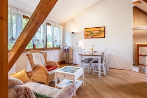 Une pièce chaleureuse comprenant un coin repas, une chaise en osier, une petite table et un tableau accroché au mur.