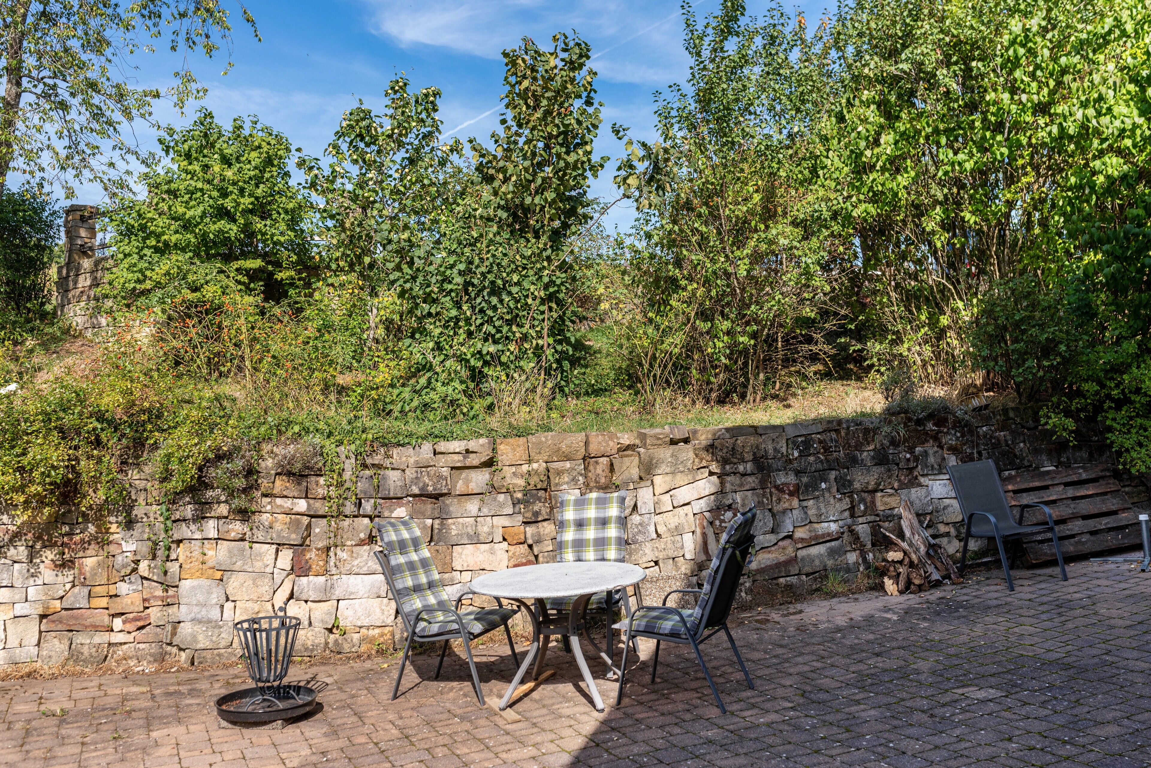 An outdoor patio with a stone wall, a round table, and four chairs.