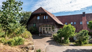 A rustic wooden building with a sloped roof, a large glass entrance, and a paved driveway. - Holiday Apartment Rose with Mountain View, Shared Terrace and Wi-Fi (Weilheim)