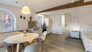 A modern kitchen with white cabinets, a dining table with chairs, and a wooden ceiling beam. - Appartment Kutscherstube (Altensteig)